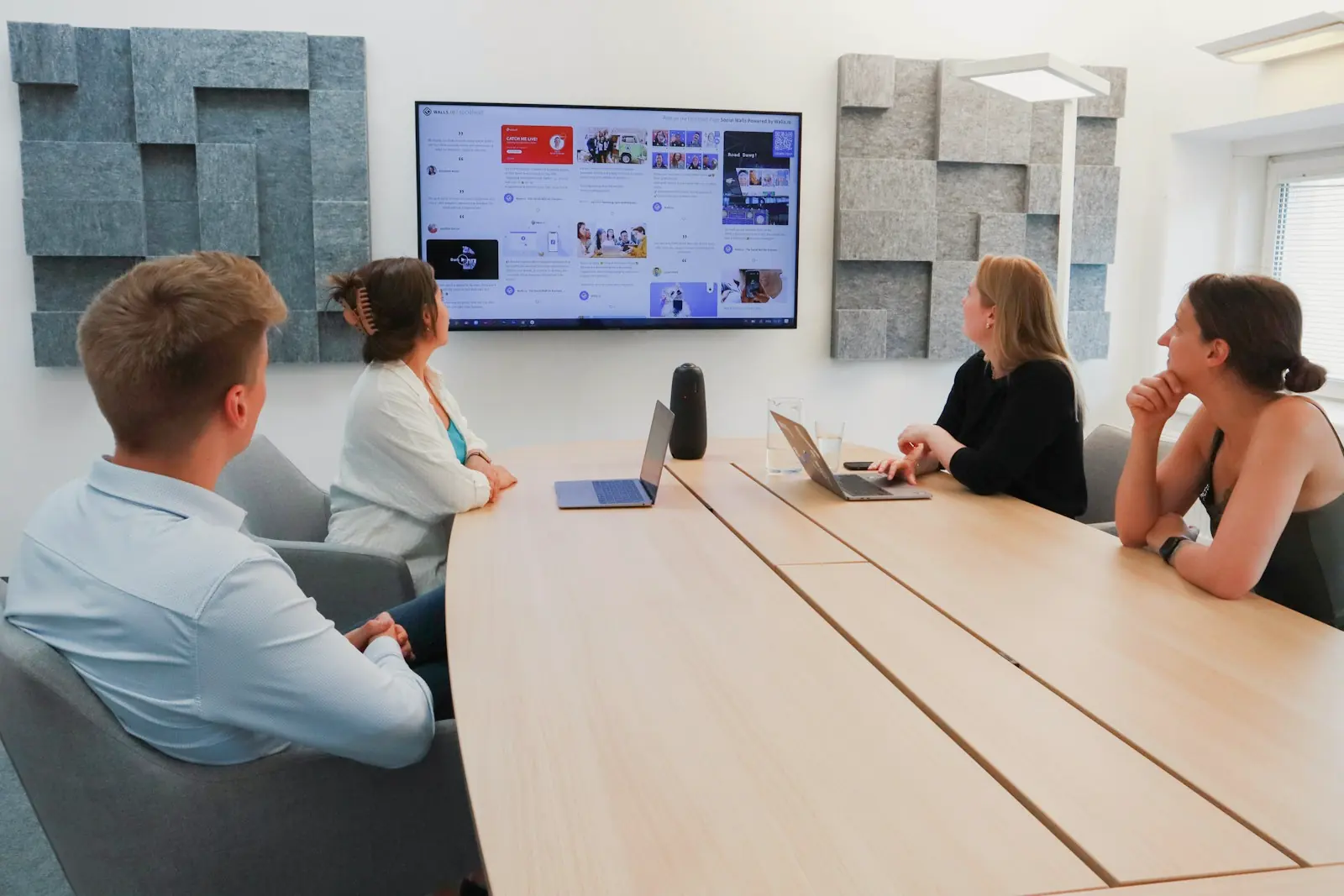 A group seated around a meeting-room table watching a presentation on a wall screen